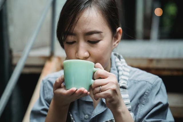 Woman in blue shirt drinking mug of warm beverage