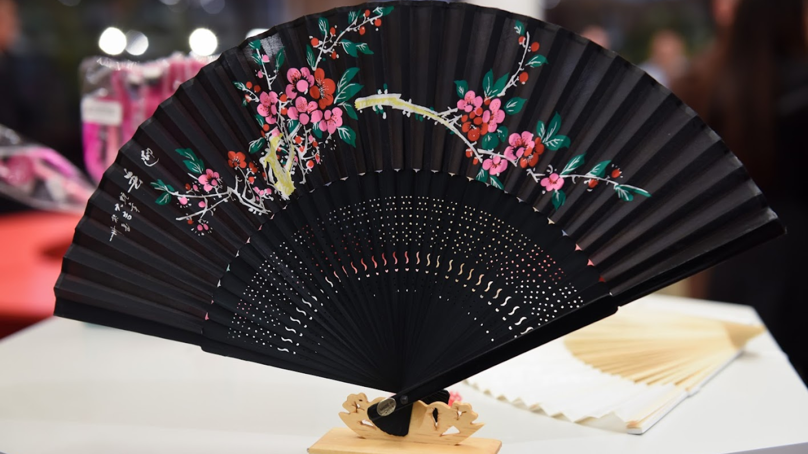 Display of black fan with pink flowers on shelf